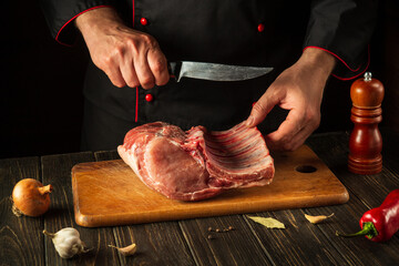 For a fire, raw ribs must be cut into small pieces. Hands of a chef with a knife in the kitchen. Cooking delicious food for a restaurant.