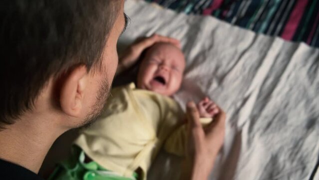 Caring father gently strokes head of upset cute crying newborn baby. Parenting issues, fatherhood concept. POV.
