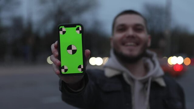 Man showing smartphone with empty green screen chromakey in a night city