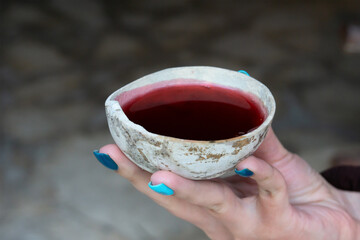A woman's hand holds a bowl with a red Mayan ritual drink. Ancient shell with hibiscus tea.