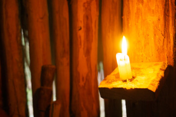 Blurred burning candle on the background of a dilapidated wooden wall. Candle flame out of focus. Lighting in an ancient hut.