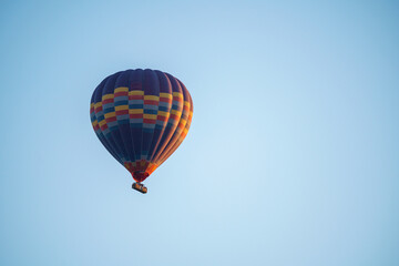 Naklejka premium Colorful balloon flying over a clear blue sky during a sunset on a sunny day in Cappadocia, Turkey, copy space