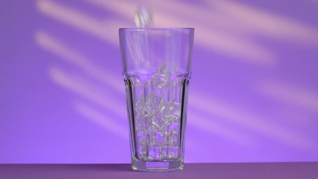 An empty glass is filled with ice on a purple background with yellow stripes
