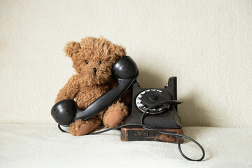 Children's teddy brown bear sits near the old phone at home and is sad, retro phone