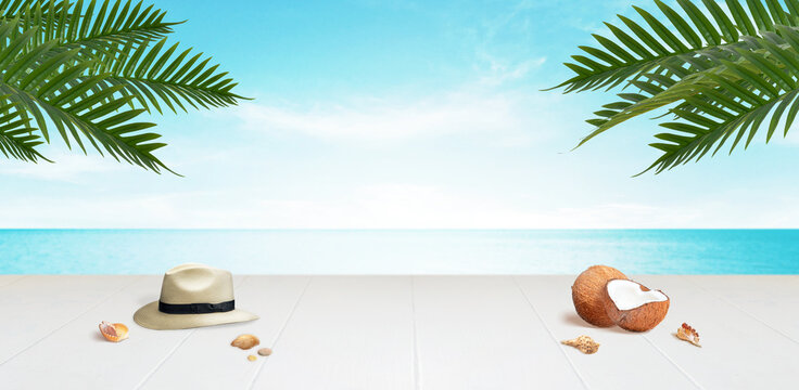 Travel background with copy space in the middle. Desk with traveler hat, coconuts and shells with palm leaves above.