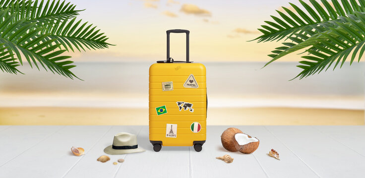 Suitcase with travel stickers on beach surrounded by hat, coconuts, shells and palm leaves. Travel concept
