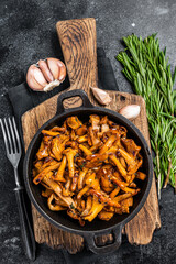 French roasted  chanterelle mushrooms with onions and thyme in a pan. Black background. Top view - obrazy, fototapety, plakaty