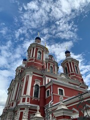 Fototapeta na wymiar Beautiful orthodox church with a chapel in the city with amazing clouds and sky. Bottom view, elongated religious building. The church is red and white with golden domes.