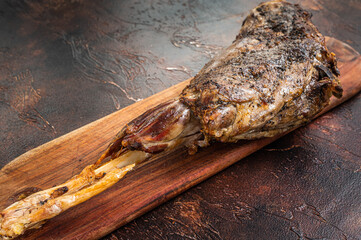 Roast lamb leg meat with herbs and spices on a cutting board. Dark background. Top view