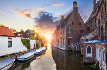 Bruges, Belgium. Medieval ancient houses made of old bricks at water channel with boats in old town. Summer sunset with sunshine. Picturesque landscape.