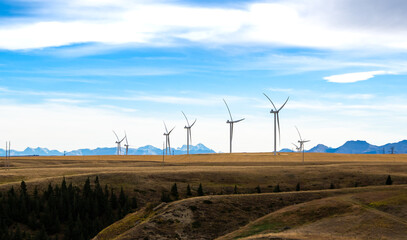 Wind turbines standing tall generating electricity with the Canadian Rocky Mountains at background...