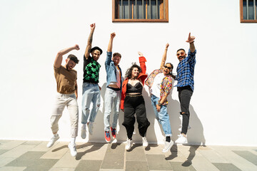 Group of happy young friends having fun and laughing, jumping over white wall. Diverse millennial people spending time together. Friendship concept