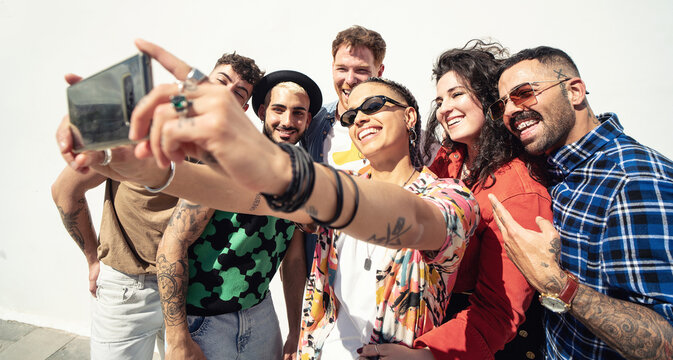 Group of happy young friends having fun and laughing while taking a selfie with mobile phone. Diverse millennial people spending time together.