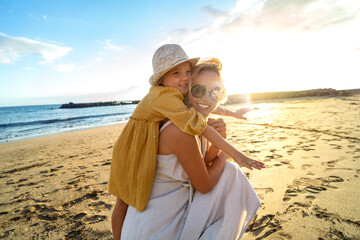 Happy mother and her little daughter having fun together on the sandy beach during sunset. Lovely...