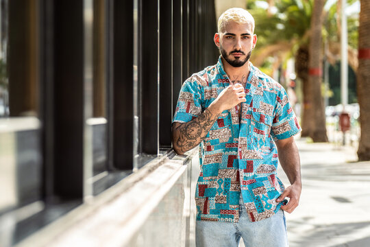 Portrait of handsome young man in casual clothing looking at camera, posing outdoor. Fashionable guy with tattoos, beard and mustache.