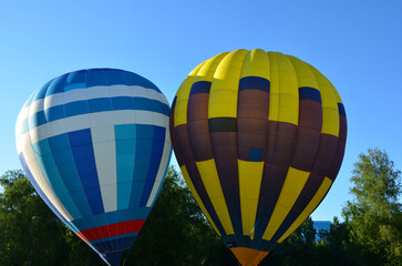 two balloons on the ground, white-blue-red and yellow-blue hot air balloon