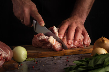 Detailed view of hands cutting through raw meat on a wooden surface with onions and herbs adjacent.