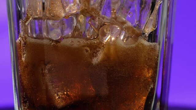 Close-up of a carbonated drink pouring through cubes in a transparent rotating glass. The camera movement is directed from the bottom up