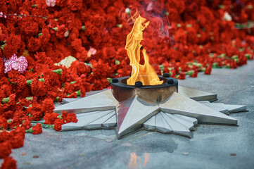 Festive background of Victory Day. Eternal flame against the background of carnations, a monument -...