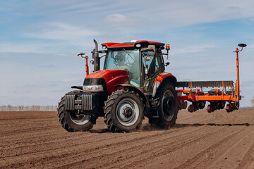 Spring sowing season. Farmer with a tractor sows corn seeds on his field. Planting corn with trailed planter. Farming seeding. The concept of agriculture and agricultural machinery.