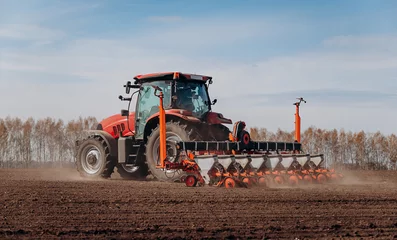  Spring sowing season. Farmer with a tractor sows corn seeds on his field. Planting corn with trailed planter. Farming seeding. The concept of agriculture and agricultural machinery. © bondvit