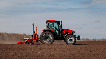 Obraz premium Spring sowing season. Farmer with a tractor sows corn seeds on his field. Planting corn with trailed planter. Farming seeding. The concept of agriculture and agricultural machinery.