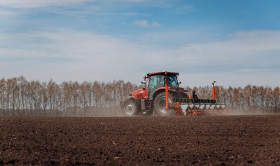 Obraz premium Spring sowing season. Farmer with a tractor sows corn seeds on his field. Planting corn with trailed planter. Farming seeding. The concept of agriculture and agricultural machinery.