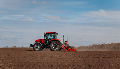 Obraz premium Spring sowing season. Farmer with a tractor sows corn seeds on his field. Planting corn with trailed planter. Farming seeding. The concept of agriculture and agricultural machinery.