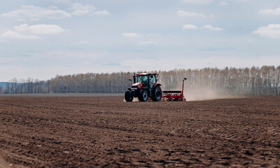 Obraz premium Spring sowing season. Farmer with a tractor sows corn seeds on his field. Planting corn with trailed planter. Farming seeding. The concept of agriculture and agricultural machinery.