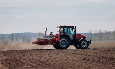 Spring sowing season. Farmer with a tractor sows corn seeds on his field. Planting corn with...