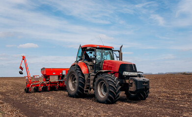 Spring sowing season. Farmer with a tractor sows corn seeds on his field. Planting corn with trailed planter. Farming seeding. The concept of agriculture and agricultural machinery.