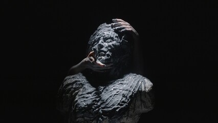 A white statue of a man. Women's hands smear paint all over the statue. A close-up shot on a black...
