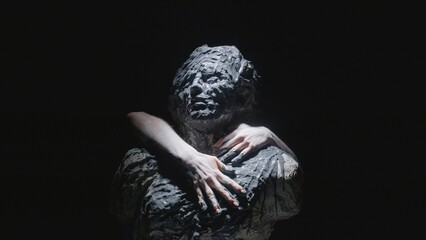 A white statue of a man. Women's hands smear paint all over the statue. A close-up shot on a black background.