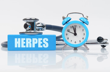 On a white surface there is an alarm clock, a stethoscope and a blue block with the inscription - HERPES