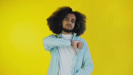 An African-American man looks at the camera, gives a thumbs down, stands isolated on a yellow...