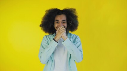 Fototapeta na wymiar A young man with an Afro hairstyle on a yellow background is happy. Emotions on a colored background.