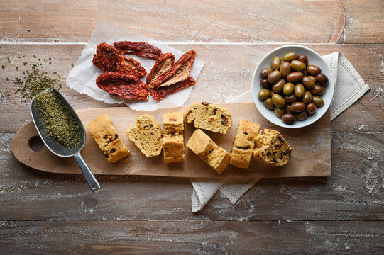 Savory biscuits, with Taggiasca olives, oregano and dried tomatoes on old rural kitchen pastry board, top view, copy space.