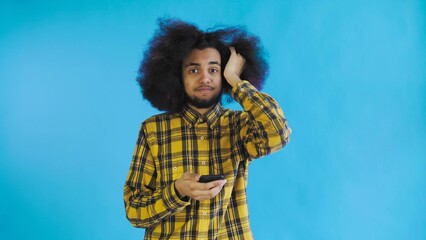 A young man with an African hairstyle on a blue background is talking into his phone.