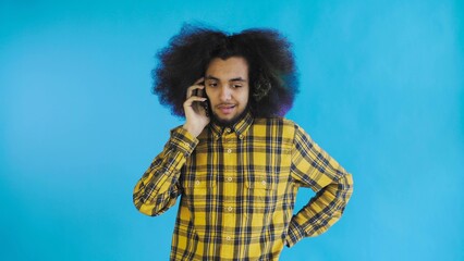 A young man with an African hairstyle on a blue background is talking on the phone. On a colored background