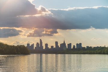 Big city skyline sunny cloudy day in Warsaw, Poland in spring, high buildings skyscrapers on horizon over Wisla river surface. Downtown beautiful cityscape panorama lit with warm sunset light