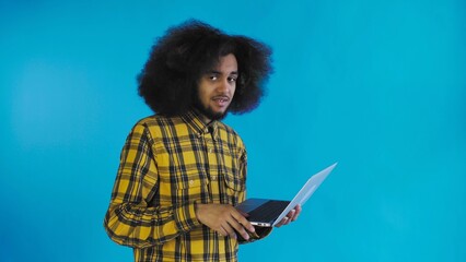 A young man with an African hairstyle on a blue background is typing on a laptop. On a colored background