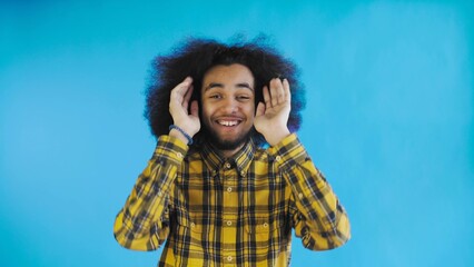A young man with an African hairstyle on a blue background is happy. Emotions on a colored background.