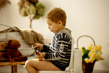 Cute toddler child, boy, using potty at home, while playing with toys