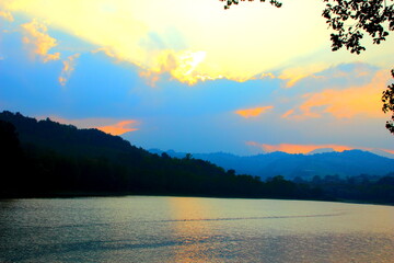 Fantastic scenery with sunbeams breaking through clouds in the sunset sky over the quiet waters of San Ruffino lake surrounded by hills covered with thickets of trees