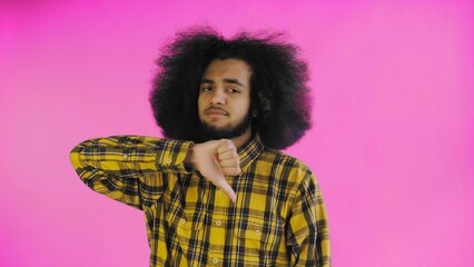 An African-American man looks at the camera, gives a thumbs down, stands isolated on a pink...