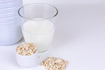 A glass of white oat milk and oatmeal flakes on white background. with copy space Vegetable milk