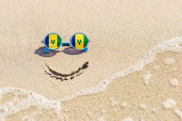 A painted smile on the sand and sunglasses with the flag of Saint Vincent and the Grenadines. The...