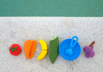 Fototapeta na wymiar fruits of toys with the colors of the LGTBIQ+ collective flag on the edge of a swimming pool.