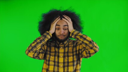 A young man with an African hairstyle on a green background is surprised. Emotions on a colored background.