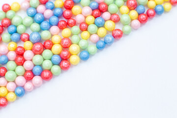 Multi-colored round glossy balls of sugar confectionery lie diagonally to the left on a white background.